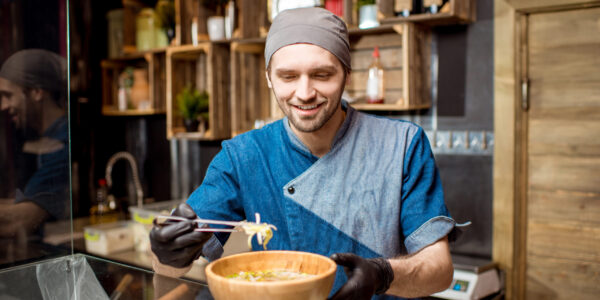 Portrait of caucasian chief cook in uniform decorating meal in the wooden plate at the asian restaurant kitchen